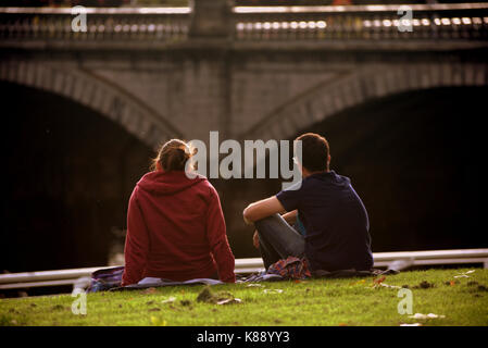 Touristische Paare sitzen auf dem Gras am Ufer des Flusses Clyde Glasgow Schottland Stockfoto