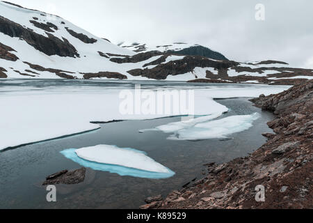 Typisch norwegische Landschaft mit schneebedeckten Bergen und Clear Lake in der Nähe der berühmten Aurlandsvegen (Bjorgavegen), Mountain Road, Aurland, Norwegen. Stockfoto