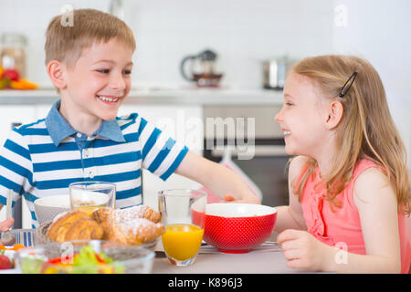 Zwei glückliche Kinder frühstücken in der Küche am Tisch Stockfoto