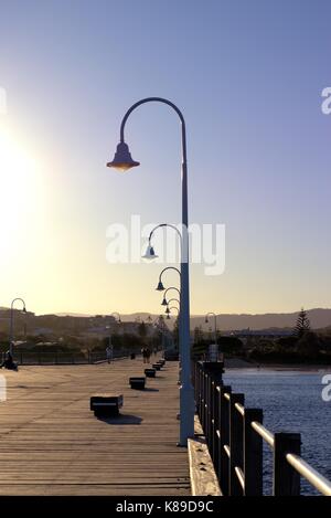 Sonnenuntergang an der Anlegestelle in Coffs Harbour, New South Wales, Australien. Im Blick sind Straßenlaternen Pole, street lamp Pole, Holzbänke. Stockfoto