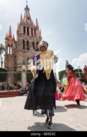 Riesige Pappmaché-Puppen namens Mojigangas tanzen vor der Kirche Parroquia de San Miguel Arcangel während einer Kinderparade, die den mexikanischen Unabhängigkeitstag feiert 17. September 2017 in San Miguel de Allende, Mexiko. Stockfoto