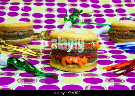 Dessert Hochstapler mock Cheeseburger und Hamburger mit Vanilla Cupcake bun- und brownie Burger auf lila Polka Dots mit bunten Luftschlangen. Stockfoto