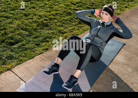 Junge Frau dabei knirscht für die Bauchmuskeln im Freien in Stockfoto