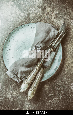 Essen Hintergrund im Vintage Style. Platte, vintage Besteck für Fleisch, Serviette mit Ring auf Stein grau hinterlegt. Ansicht von oben, getönt. Stockfoto