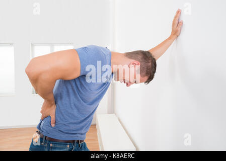 Junger Mann mit Rückenschmerzen während lehnte sich auf weiße Wand Stockfoto