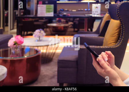 Der weibliche Hände mit einem mobilen Touchscreen Handy in der Lobby Stockfoto