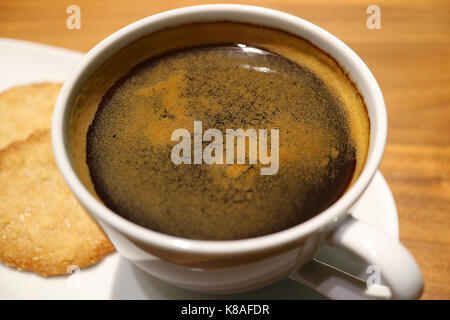 Geschlossen bis eine Tasse schwarzen Kaffee in eine weiße Tasse mit einige Cookies serviert, selektiver Fokus Stockfoto