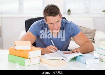 Junger Mann Bücher lesen am Schreibtisch im Wohnzimmer. Stockfoto