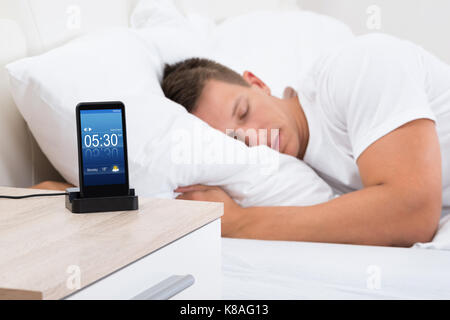 Junger Mann schläft auf dem Bett mit Alarm auf Handy-Display Stockfoto