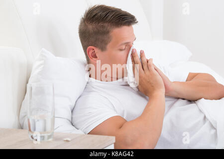 Junger Mann im Bett bläst seine Nase in Taschentuch Stockfoto