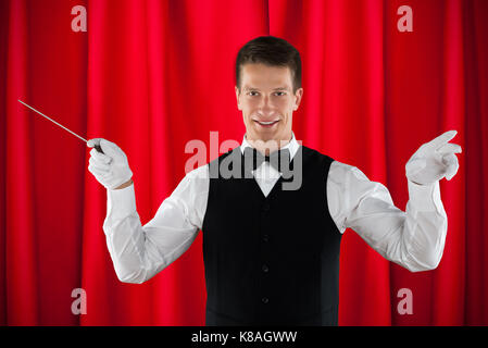 Männliche Orchester Dirigent Holding Baton über den roten Vorhang Stockfoto