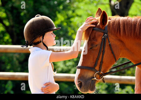 Ein junges Mädchen mit einem Pony oder Pferd, Betreuung und Pflege die Tier auf einem Reiterhof Schule einstellen Tack und Satteln in Vorbereitung für das Reiten. Stockfoto