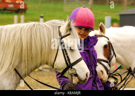 Ein junges Pferd Reiter auf der Suche nach und halten zwei Pferde oder Ponys tragen, Kit und lächelnd die Pflege der Tiere. Stockfoto