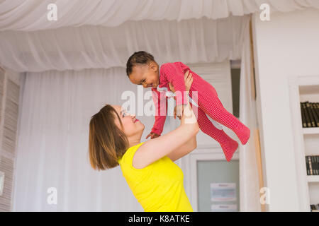 Glückliche Familie. Mutter wirft durcheinander Rennen Baby, zu Hause spielen Stockfoto