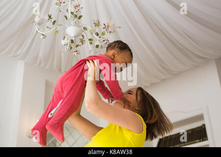 Glückliche Familie. Mutter wirft durcheinander Rennen Baby, zu Hause spielen Stockfoto