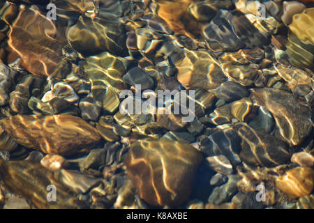 Hintergrund der glänzenden Kieselsteine am Fluss unten. Abstrakte Muster der Kieselsteine unter der Oberfläche des Wassers. Stockfoto