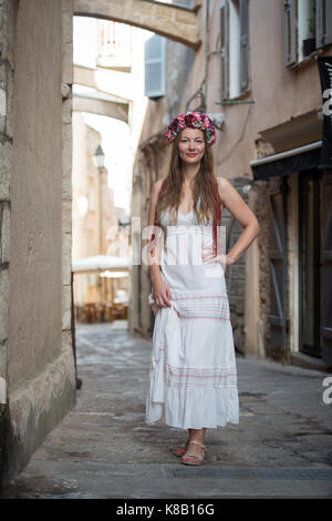 Junge Frau im weißen Kleid mit Stirnband in den Straßen von Bonifacio, Frankreich Stockfoto
