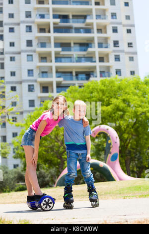 Cute girl am Hoverboard mit ihrem Bruder auf rollerblade Spaß im Freien Stockfoto