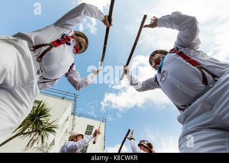 Hartley Morrismen Tänzer, in Weiß mit roten Klammern und Strohhüte gekleidet, stehend über Viewer, bashing Holzpfähle. Blauer Himmel, weiße Wolken. Stockfoto