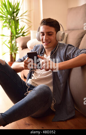 Jugendlich sitzen auf dem Boden lehnte sich auf der Couch mit einem Smartphone im Wohnzimmer. Vertikale Zusammensetzung Stockfoto