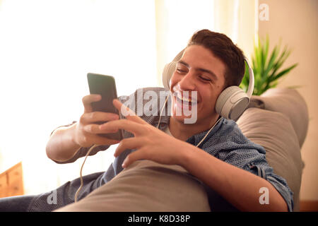 Teenager lachen Sie Multimedia-Inhalte auf ein Handy mit Kopfhörer lehnte sich auf der Couch zu Hause Stockfoto