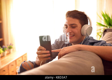 Teenager beobachten, multimediale Inhalte auf ein Handy mit Kopfhörer lehnte sich auf der Couch zu Hause Stockfoto