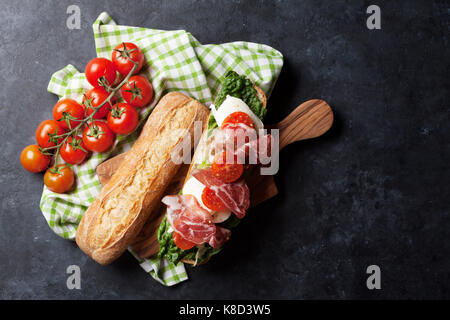 Ciabatta-Sandwich mit Salat, Schinken und Mozzarella Käse Romaine über Stein Hintergrund. Ansicht von oben Stockfoto