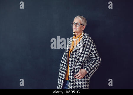 Stilvolle alte Frau in Gläser, stehend auf einem schwarzen Hintergrund. Stockfoto