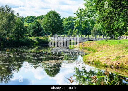 Alte steinerne Brücke mit Bögen über schmalen Flusses in der Waldlandschaft. Lage Vissefjarda in Südschweden. Stockfoto