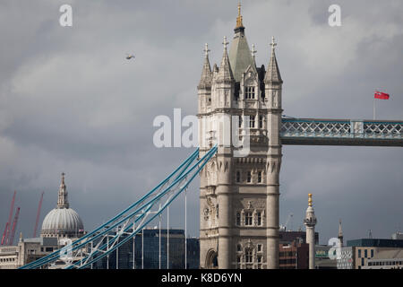 Eine Metropolitan Polizei Hubschrauber Patrouillen der Himmel über der Kuppel der St. Paul's Kathedrale (links), der goldene - erstklassige Monument (rechts) und in der Mitte, im Süden main tower der viktorianischen Ära Tower Bridge, am 14. September 2017 in London, England. Stockfoto