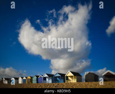 Eine riesige weiße Wolke vor blauem Himmel ragt über eine Reihe von bunten Holzhütten am Calshot Hampshire England Stockfoto