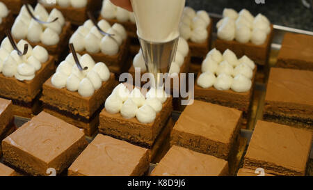 Creme auf Schokolade Kuchen gequetscht wird. Quetschen Sie die Sahne auf dem Kuchen Stockfoto