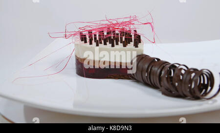 Torte mit drei Schichten auf einem Teller. Torte mit drei Schichten, dekoriert mit Schokolade Krümel und Schokolade Stroh Stockfoto