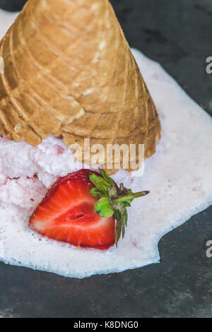 Erdbeereis in Waffle Kegel invertiert und gegen einen dunklen Hintergrund geschmolzen, close-up. Stockfoto