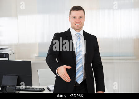 Portrait von Happy Geschäftsmann mit Handshake beim Stehen bei Computer Schreibtisch im Büro Stockfoto