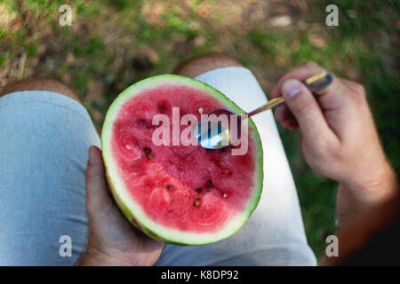 Ein junger Mann ist das Essen eine Wassermelone mit einem Löffel. Das Konzept der gesunden Ernährung und Vegetarismus. Stockfoto