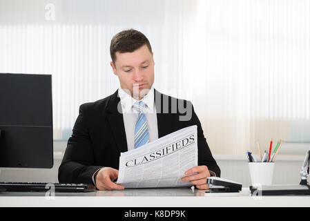 Geschäftsmann lesen Zeitung, beim Sitzen am Schreibtisch im Büro Stockfoto