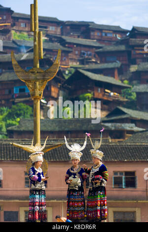 Xijiang, China - September 15, 2007: Drei ethnischen Minderheit Miao Frauen in traditioneller Kleidung und Silber Kopfschmuck stand auf Stadtplatz Holzhäuser o Stockfoto