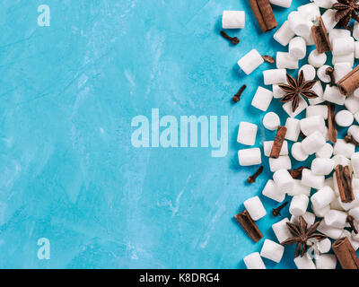 Marshmallows und Winter Gewürze auf blauem Hintergrund mit Copyspace. Flach oder der Ansicht von oben. Hintergrund der bunten mini Marshmallows, Zimt, Nelken und Stockfoto