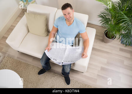 Hohe Betrachtungswinkel und der Mitte der erwachsene Mann Lesen der Zeitung auf dem Sofa zu Hause Stockfoto