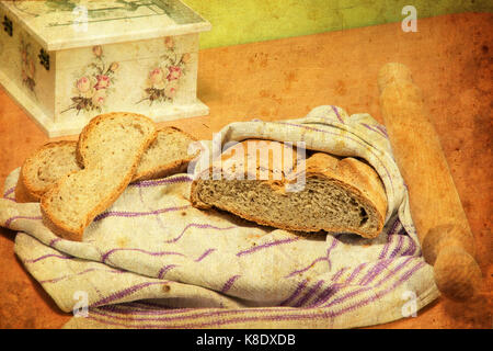 Brotlaib in Küche Tuch eingewickelt, zwei Scheiben Brot, und Rolling Pin. Decoupage Box ist teilweise sichtbar. Vintage Look. Selektive konzentrieren. Stockfoto