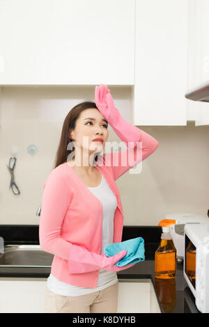 Junge Frau in rosa Gummihandschuhe Reinigung einer Oberfläche der weißen Küche, Schrank Stockfoto