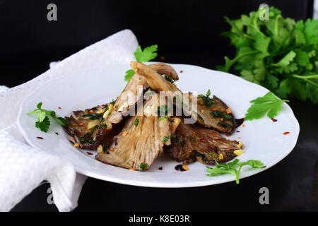 Gebratene Austernpilze mit Knoblauch, Petersilie in einer Balsamico glaze auf schwarzem Hintergrund. Gesunde Ernährung Konzept. Stockfoto