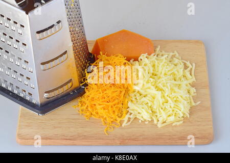 Schritt für Schritt das Kochen. Geriebenen Gouda und Cheddar Käse mit einer Reibe auf einer hölzernen Schneidebrett auf grauem Hintergrund Stockfoto