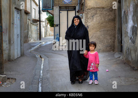 Provinz Fars, Shiraz, Iran - 18. April 2017: Lächelnde muslimische Frau in Khimar stehen im Hof, und die Hand eines kleinen Mädchens in einem rosa Dre Stockfoto