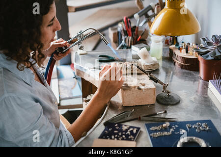 Weibliche Juwelier mit Brenner an der Werkbank Stockfoto