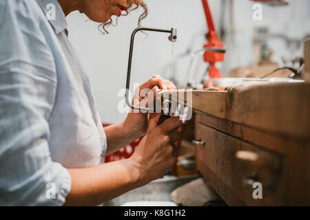 7/8-Ansicht der weiblichen Juwelier mit der Bewältigung sah in der Workbench Stockfoto