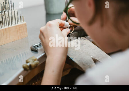 Blick über die Schulter der weiblichen Juwelier und Ring an der Werkbank Stockfoto