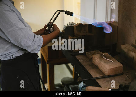 Den mittleren Abschnitt der weiblichen Juwelier mit flammenden Brenner an der Werkbank Stockfoto