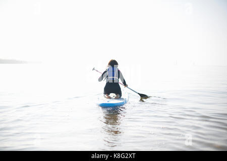 Ansicht der Rückseite des Weiblichen paddleboarder aus Paddeln auf Misty sea Stockfoto